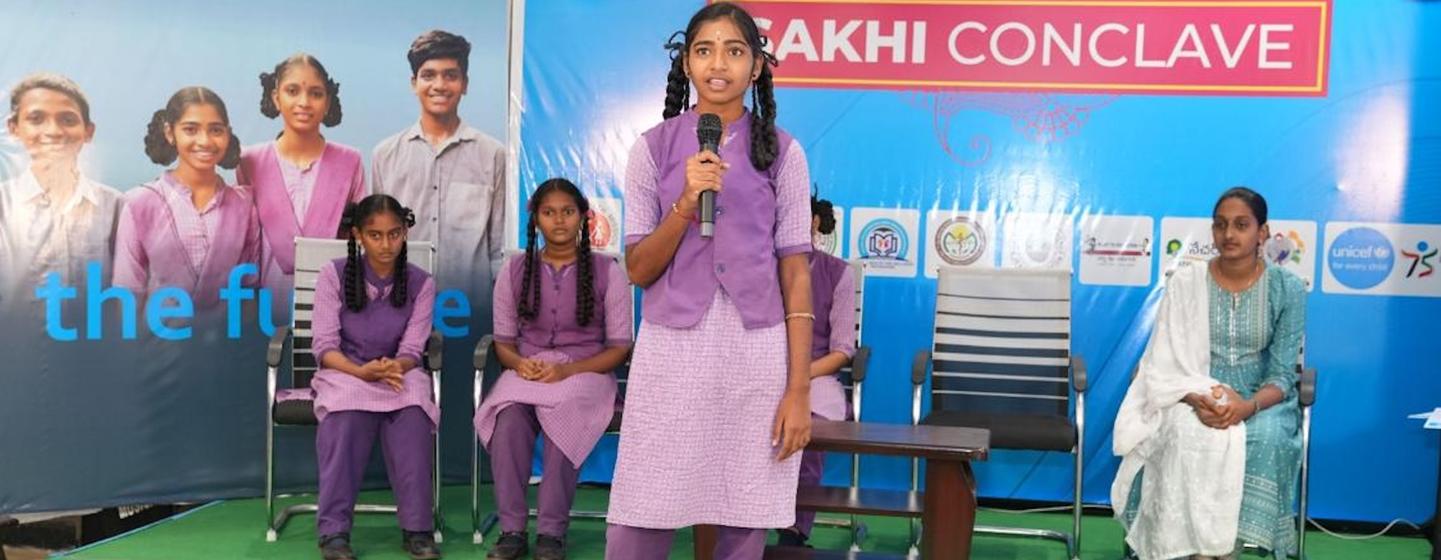 आंध्र प्रदेश में आयोजित सखी सम्मेलन में बैंगनी रंग की स्कूली वर्दी पहने एक किशोरी मंच पर माइक्रोफोन में बोल रही है।