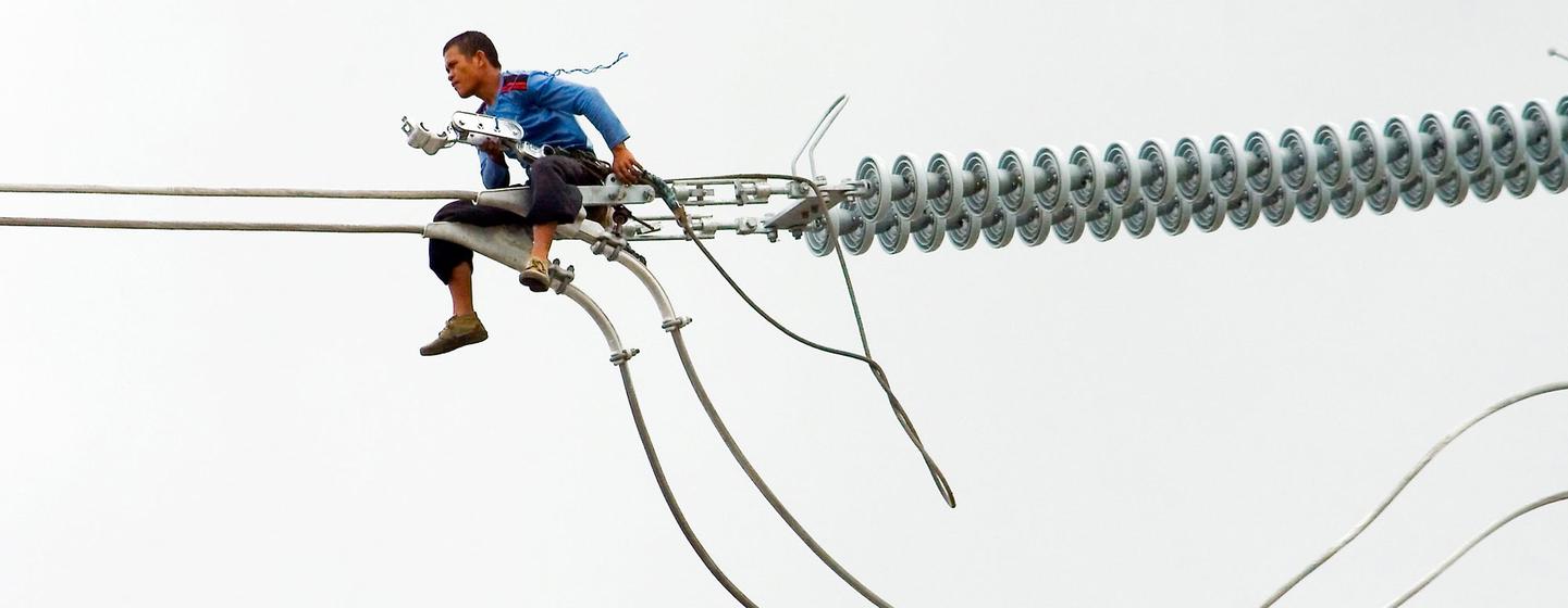 Un ouvrier installe un nouveau cable électrique en haut d'un pylone à Cavite, aux Philippines.