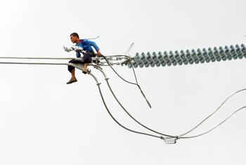 Un ouvrier installe un nouveau cable électrique en haut d'un pylone à Cavite, aux Philippines.