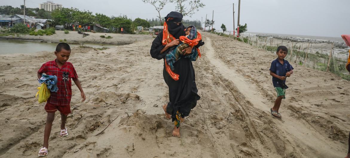 बांग्लादेश के पंजूपारा गाँव में एक महिला अपने बच्चों के साथ, चक्रवाती तूफ़ान के टकराने से पहले अस्थाई शिविर की ओर जा रही है. (26 मई 2024)