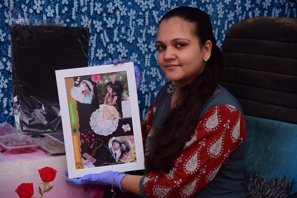 नीले दस्ताने और लाल-सफेद कुर्ते में सजी कविता गुसानी ने एक खास डिज़ाइन का स्क्रैपबुक फोटो फ्रेम पकड़ा हुआ है। वह नीले फूलों की पृष्ठभूमि वाले रैग्स टू रनवे कार्यक्रम में मौजूद हैं।