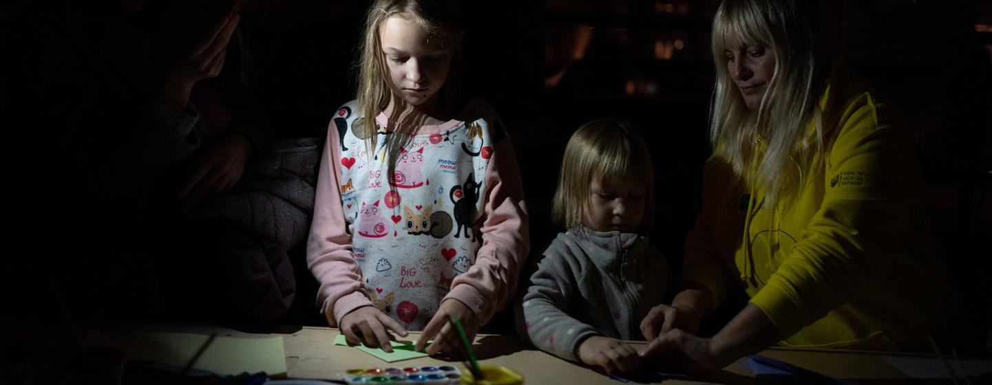 Une femme et deux enfants peignent à l'aquarelle sur une table à l'intérieur d'une station de métro obscure.