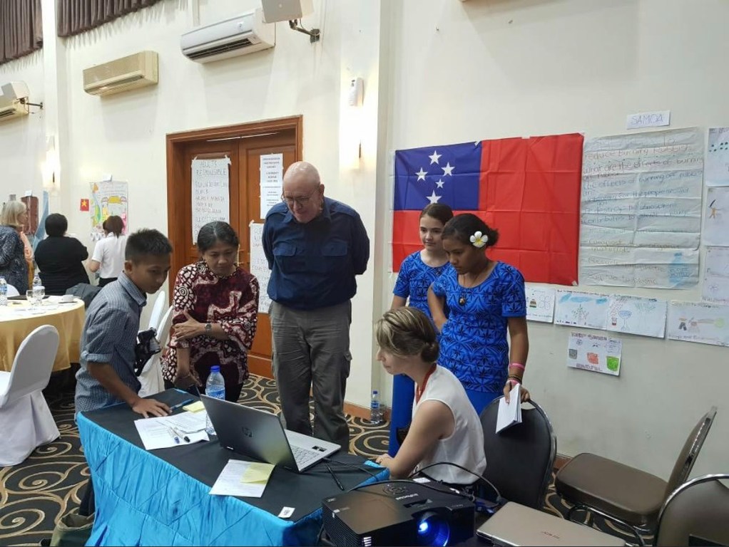 Un grupo de personas, entre ellas un hombre, una mujer y niños, se reunieron alrededor de una mesa con un ordenador portátil y un proyector en un evento.
