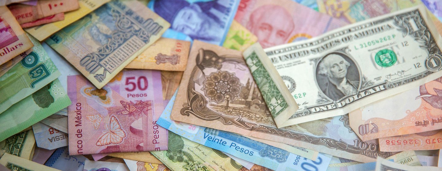 Uma variedade colorida de diversas notas e moedas internacionais de diferentes países espalhadas sobre uma superfície.