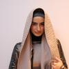 Une mannequin portant un hijab beige et une veste à paillettes lors d'un événement de mode.