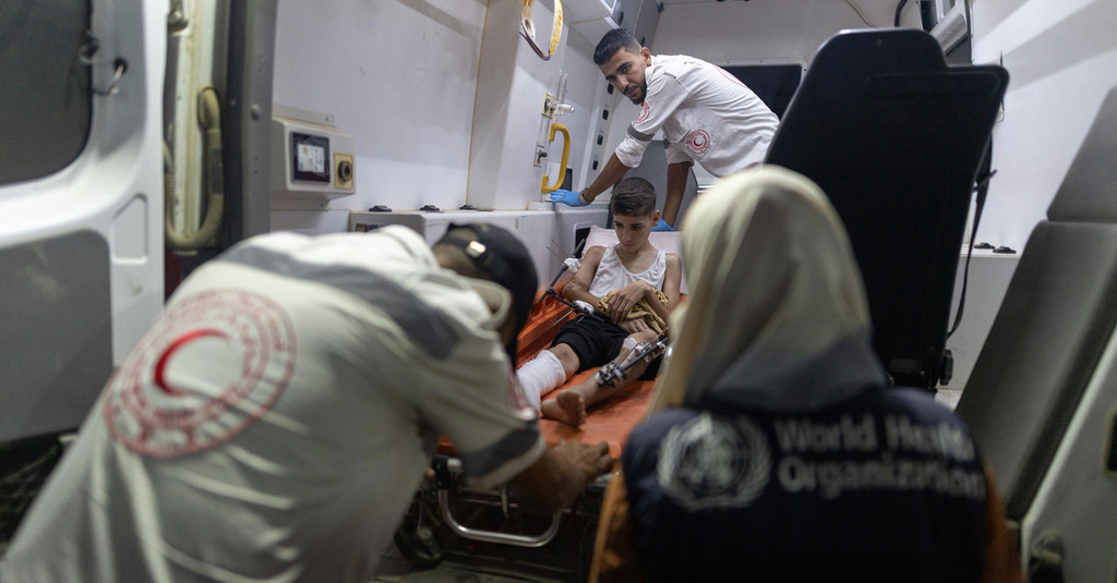 Un niño palestino con un yeso en la pierna es cargado en una ambulancia por personal médico vestido con uniformes de la Media Luna Roja.