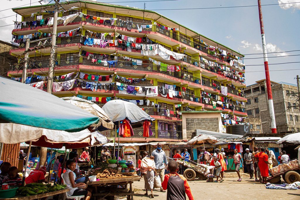 Um prédio de apartamentos de vários andares, com lavanderias nas varandas, tem vista para um movimentado mercado de rua na favela de Mathare, em Nairóbi, Quênia.