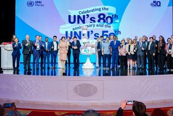 一群身着正装的人们在联合国成立 80 周年暨联合国大学成立 50 周年纪念活动上登台庆祝。