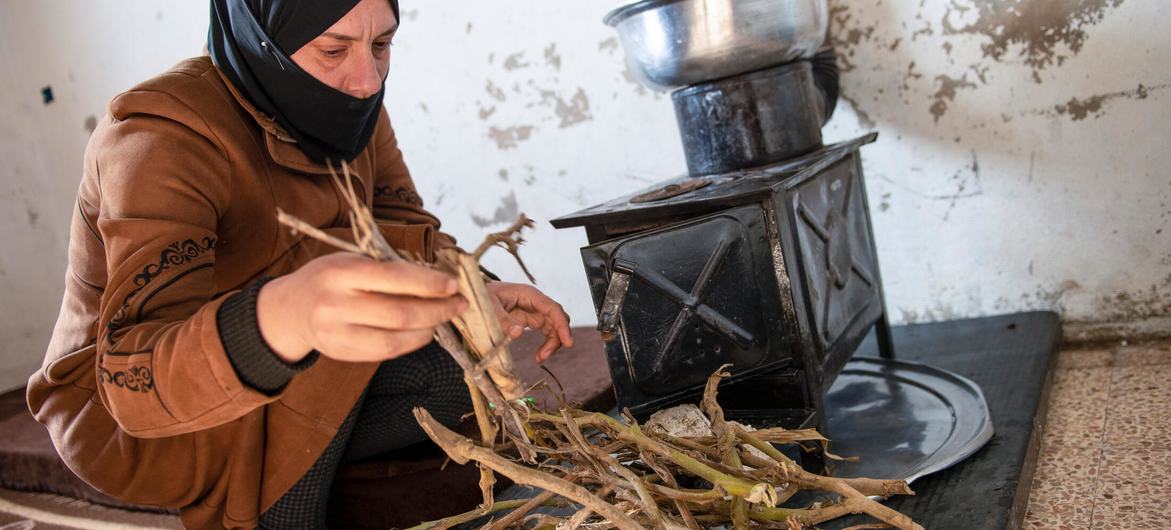 A woman feeding twigs to a heater to warm her house in rural Damascus.
