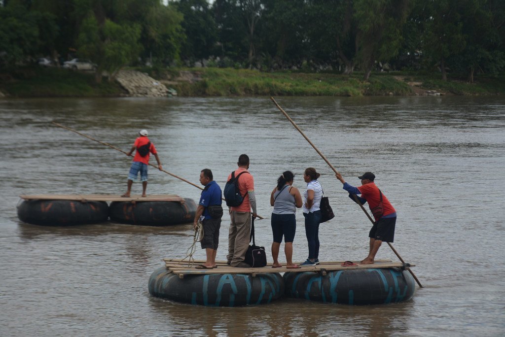 Un grupo de personas se encuentra de pie sobre balsas en el río Suchiate mientras cruzan la frontera entre Guatemala y México.