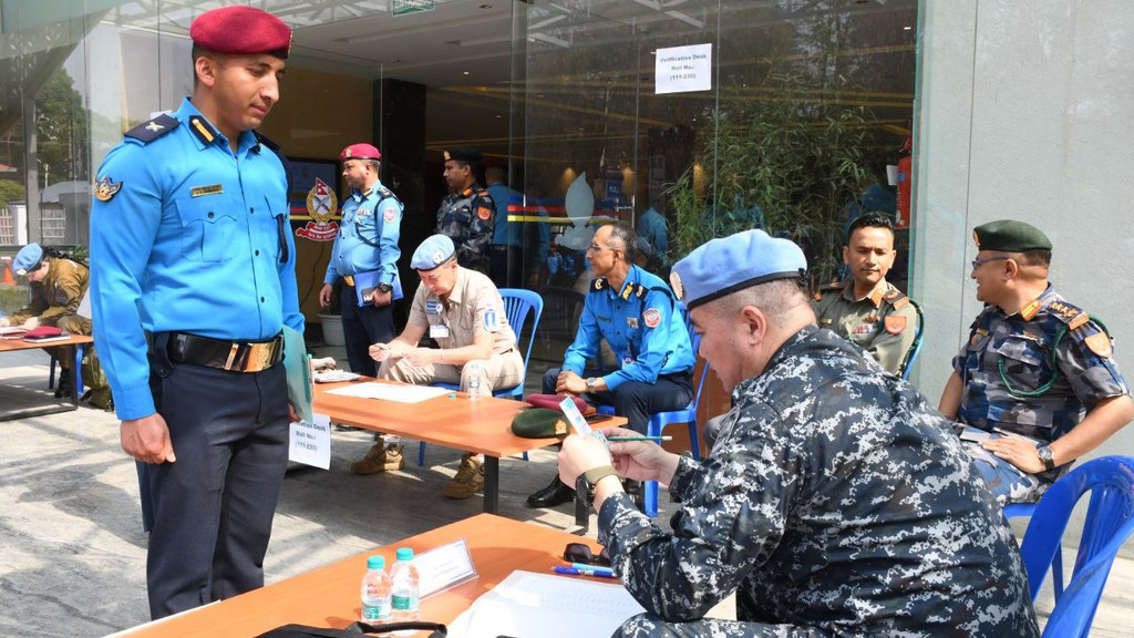 Военнослужащие в форме ООН и гражданской одежде у регистрационной стойки возле здания.