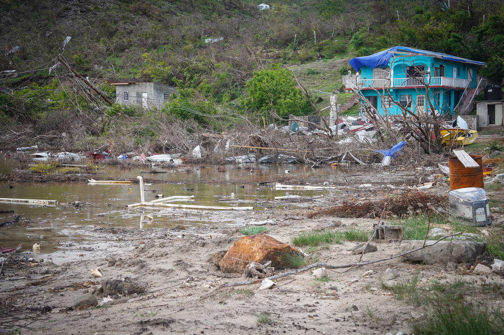 Una costa inundada y llena de escombros en Union Island, Caribe, que muestra las consecuencias del huracán Beryl, con una casa turquesa dañada y un edificio de hormigón destruido.