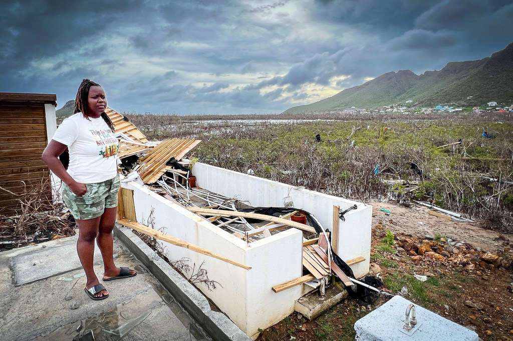 Una mujer permanece de pie sobre un patio de cemento junto a una estructura dañada en un paisaje de manglares devastado en Union Island, en el Caribe.