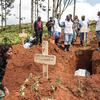 Des membres de l'équipe de spécialistes de la Croix-Rouge chargés des inhumations, vêtus de matériel de protection, assistent une femme endeuillée dans un cimetière de Butembo, en RDC, lors d'une intervention d'urgence contre Ebola. Un cercueil est descendu dans une fosse fraîchement creusée.
