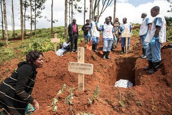 Des membres de l'équipe de spécialistes de la Croix-Rouge chargés des inhumations, vêtus de matériel de protection, assistent une femme endeuillée dans un cimetière de Butembo, en RDC, lors d'une intervention d'urgence contre Ebola. Un cercueil est descendu dans une fosse fraîchement creusée.