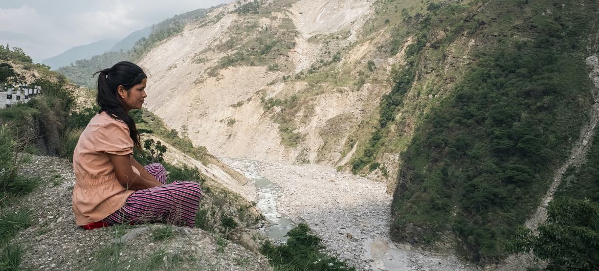 No oeste do Nepal, uma menina está sentada à beira de um penhasco, olhando para um enorme deslizamento de terra causado pelas chuvas das monções de 2023.