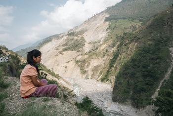 在尼泊尔西部，一个女孩坐在悬崖边，俯瞰着 2023 年季风雨带来的大规模山体滑坡。