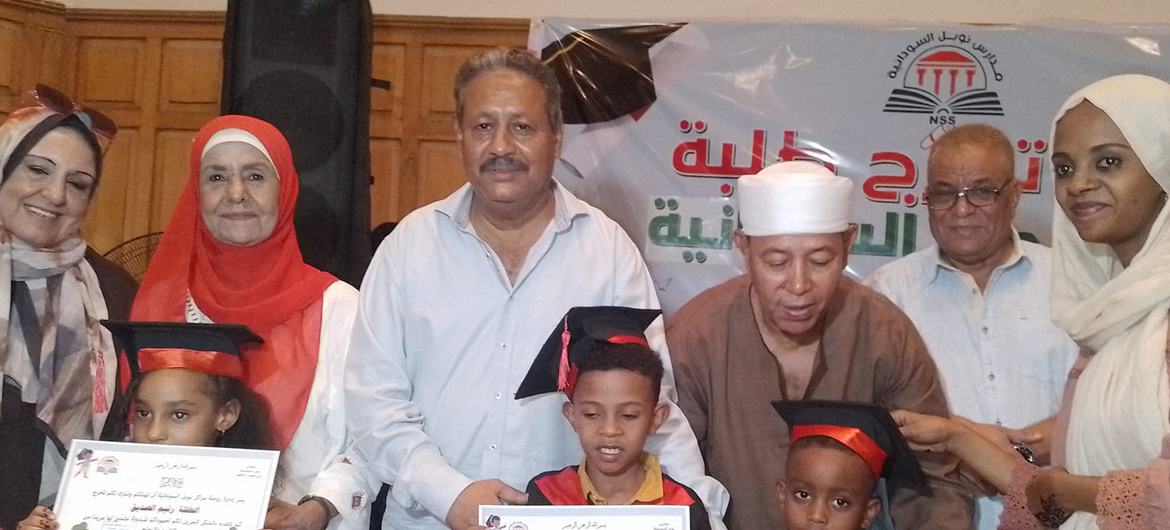 أطفال وبالغون سودانيون في حفل تخرج، يحملون شهادات التخرج.
