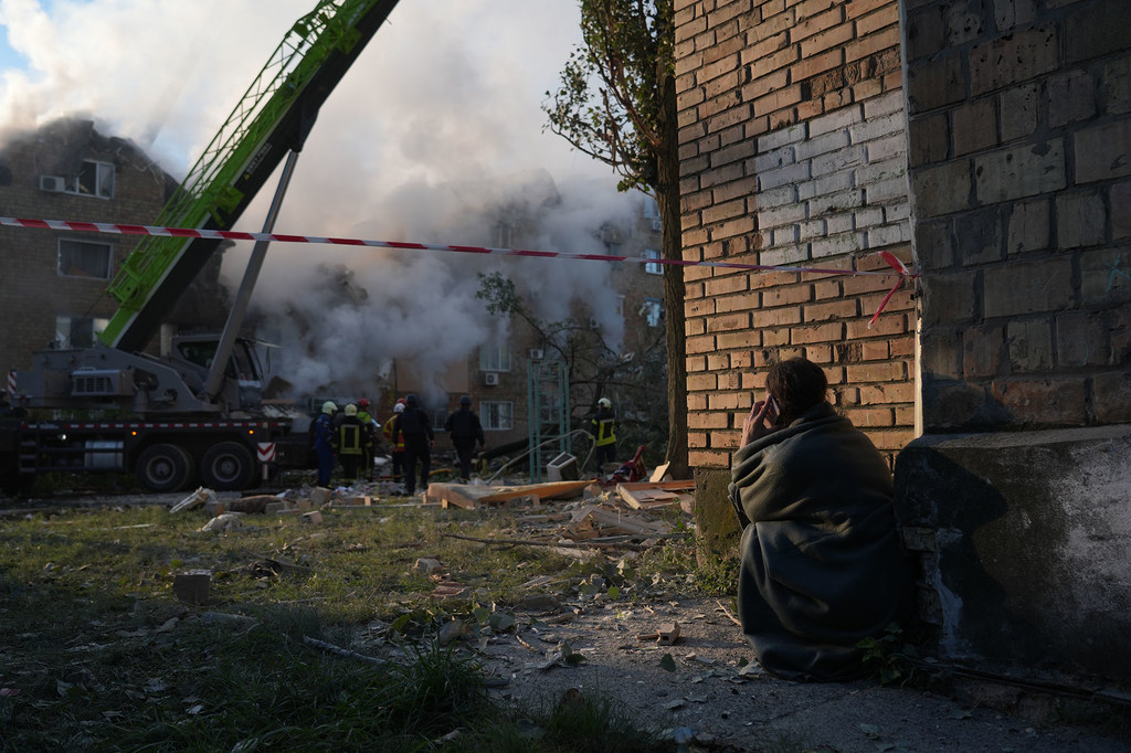 A resident near the ruins of a residential building in Kyiv, watching as emergency crews search for survivors following a missile strike in the early hours of the morning on 28 August.