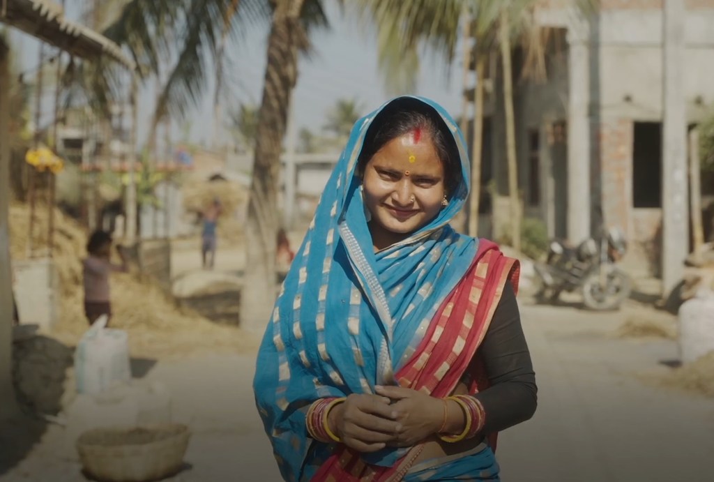 Bibha, mnufaika wa mradi wa IFAD, kutoka Nepal, akiwa amevaa sari ya bluu, amesimama katika mazingira ya kijijini.