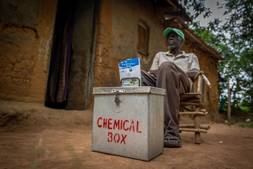 Mkulima ameketi mbele ya chombo chenye lebo ya 'KISANDUKU CHA KEMIKALI' katika mazingira ya vijijini.