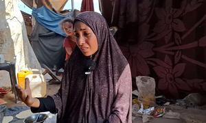 Aisha Al-Ra'i, desplazada de la ciudad de Gaza al sur de la Franja, habla a su marido herido sentado mientras ella maneja el horno de barro.