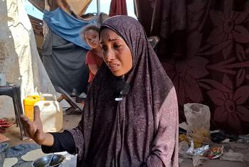 Aisha Al-Ra‘i, desplazada de la ciudad de Gaza al sur de la Franja, habla a su marido herido sentado mientras ella maneja el horno de barro.