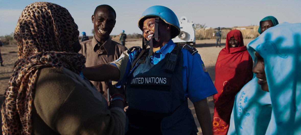 امرأة من قوات حفظ السلام United Nations ترتدي خوذة وسترة زرقاء تتحدث مع نساء عند نقطة مياه في مخيم نيفاشا للنازحين داخلياً في شمال دارفور.
