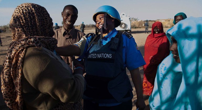 امرأة من قوات حفظ السلام United Nations ترتدي خوذة وسترة زرقاء تتحدث مع نساء عند نقطة مياه في مخيم نيفاشا للنازحين داخلياً في شمال دارفور.