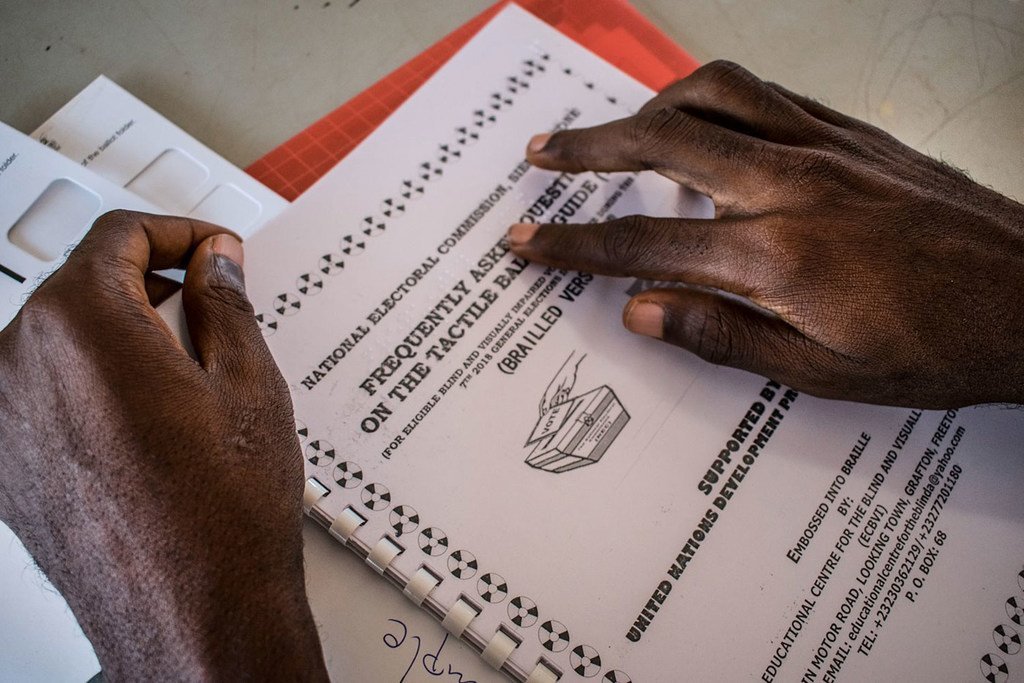 Um close-up de mãos usando um guia tátil para votação no dia da eleição em Serra Leoa.