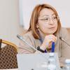 Женщина в очках сидит за конференционным столом с ноутбуком и микрофонами, на фоне видны флаги Казахстана и ВОЗ.