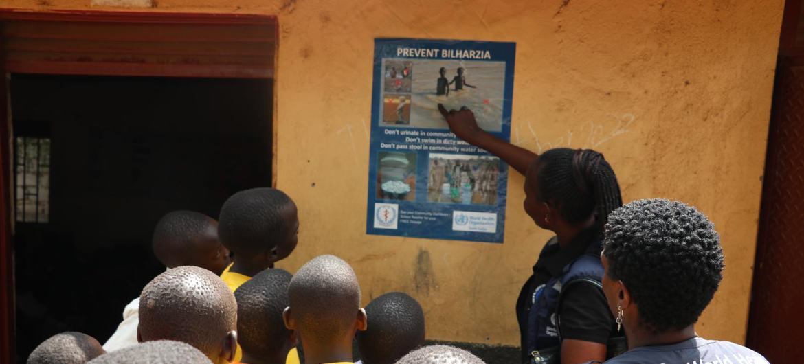 Un employé de l'Organisation mondiale de la santé montre du doigt une affiche « Prévenir la bilharziose » sur un mur où se trouve un groupe d'enfants au Soudan du Sud.