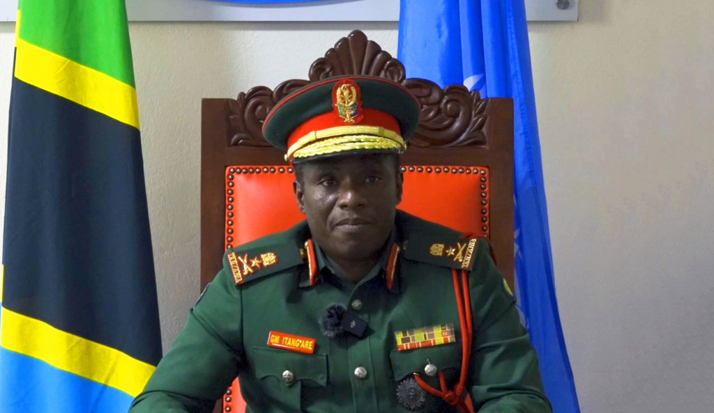 Brigedia Jenerali George Itang'are wa Chuo cha Kulinda Amani cha Tanzania ameketi kwenye kiti mbele ya Mtanzania na bendera UN .