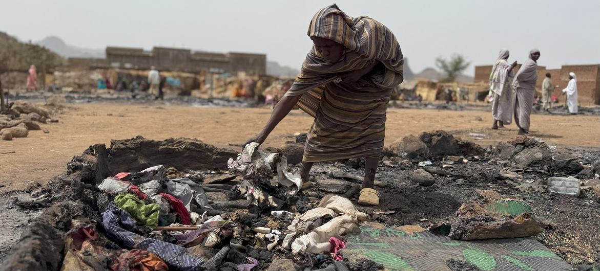 A woman searches through the burnt remains of her shelter at a displacement camp in Darfur, Sudan.