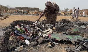 Una mujer busca entre los restos quemados de su refugio en un campo de desplazados de Darfur, Sudán.