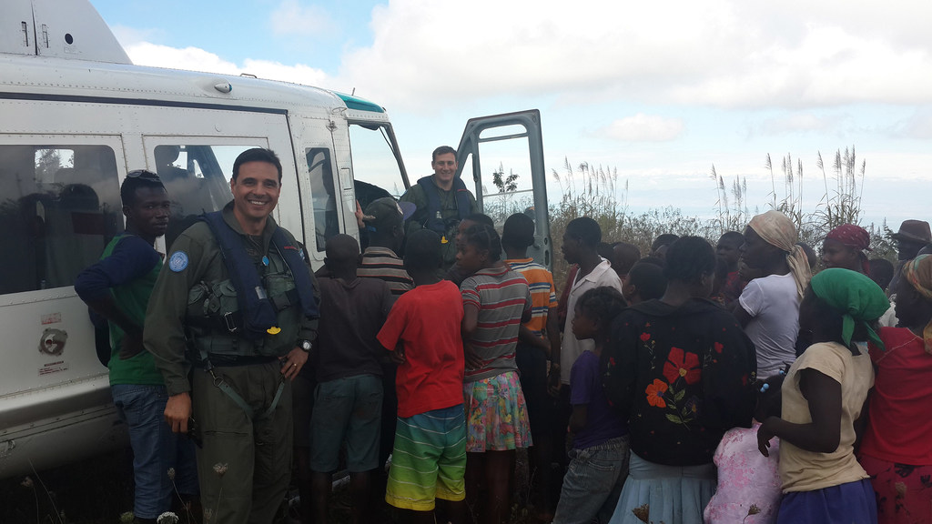 El comodoro Javier Chiappai posa frente a un helicóptero junto a una multitud de personas, entre ellas niños, en Haití.