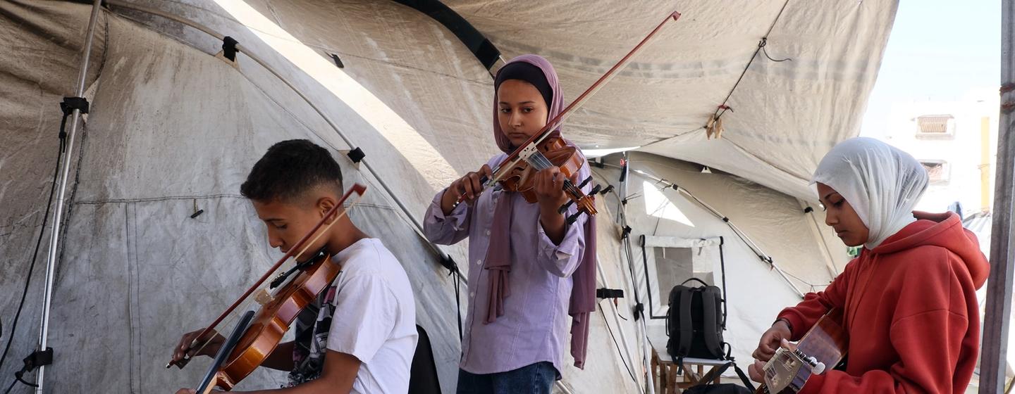 A boy and two girls playing music inside a tent in Gaza.