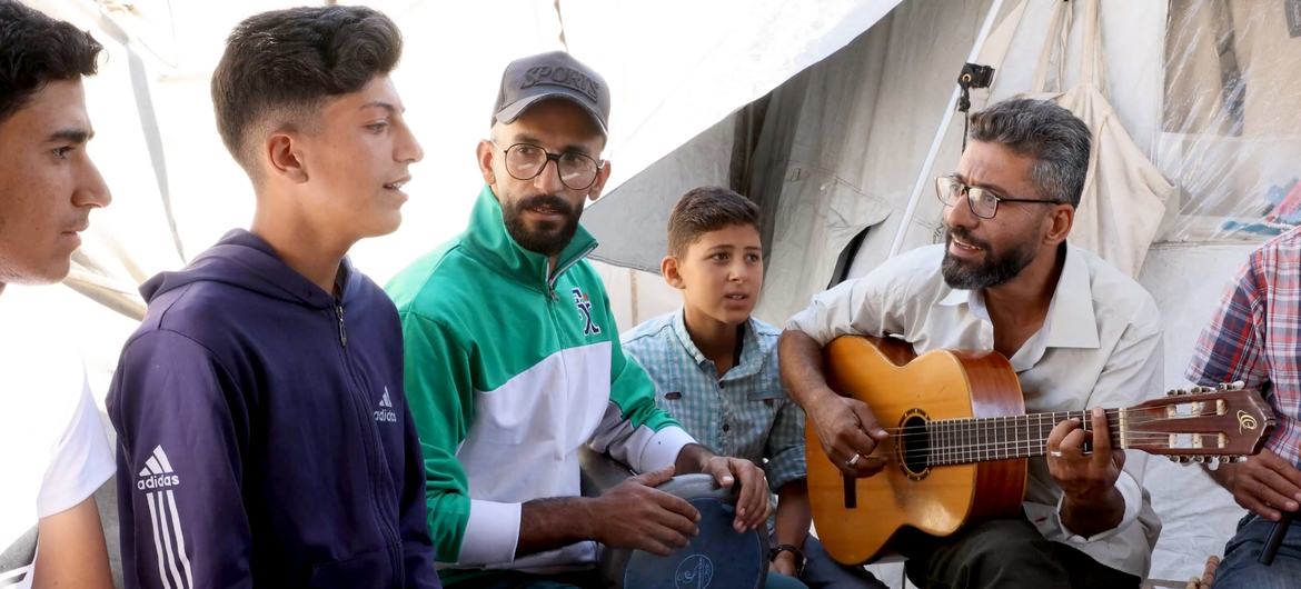 Ahmed Abu Amsha (right, with guitar) surrounded by children who play, sing and learn music. Ahmed Abu Amsha (right, with guitar) surrounded by children who play, sing and learn music.