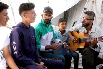 أحمد أبو عمشة محاط بالأطفال لعزف الموسيقى والغناء وتعلم الموسيقى.