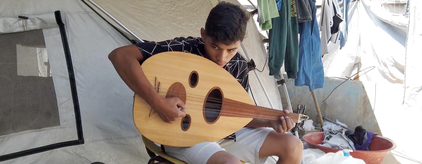Un garçon joue de la musique à l'intérieur d'une tente à Gaza.