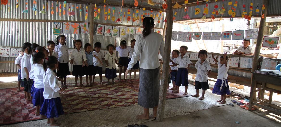 Uma professora está em uma sala de aula na zona rural do Camboja com um grupo de jovens alunos.