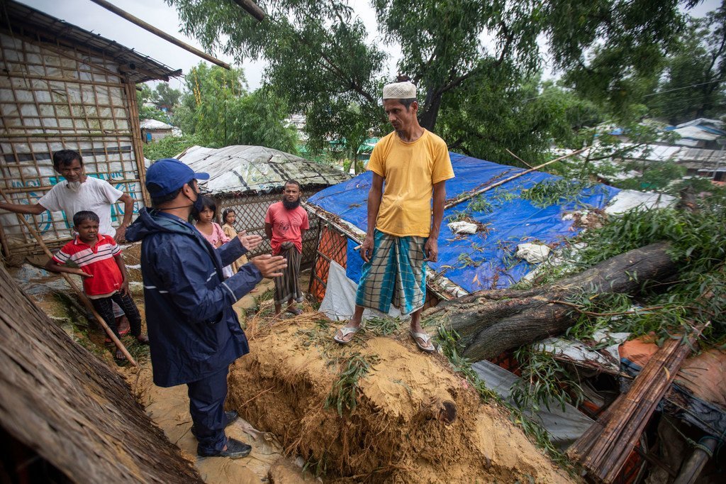 Un trabajador de la OIM, vestido con un impermeable azul, habla con un hombre rohingya en un campo de refugiados en Cox's Bazar, Bangladesh, después de que una inundación haya destruido muchos refugios.