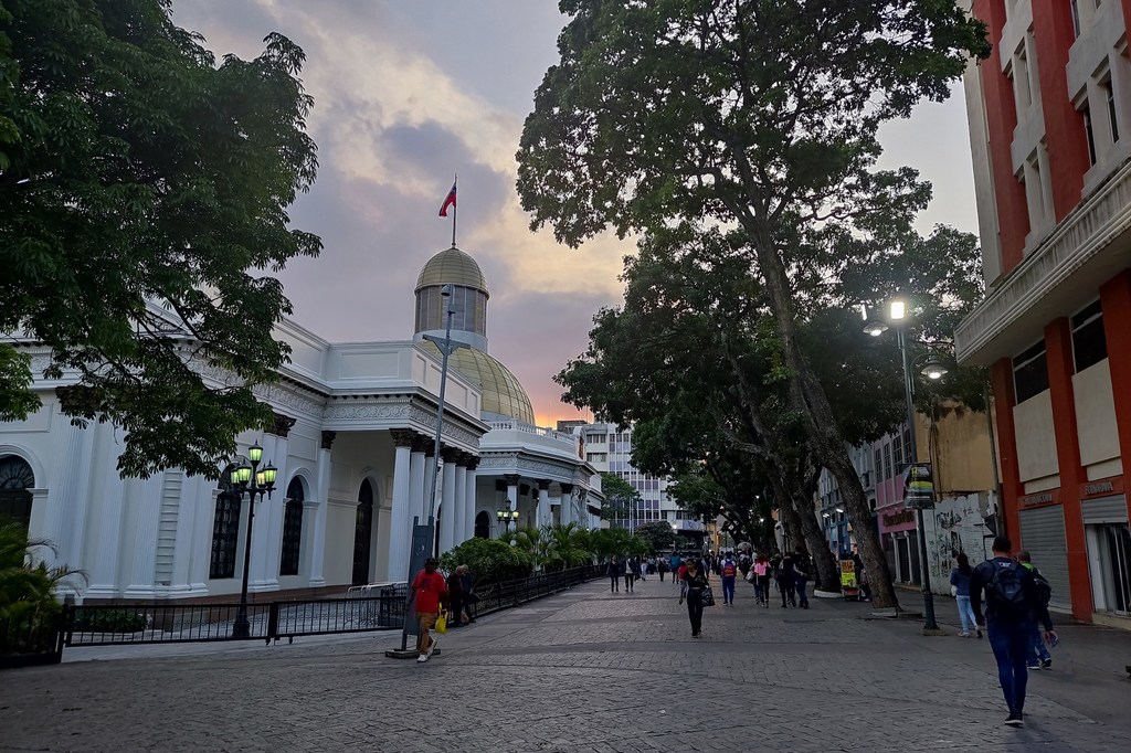 Peatones caminan por una calle empedrada frente al edificio de la Asamblea Nacional en Caracas, Venezuela, al atardecer.