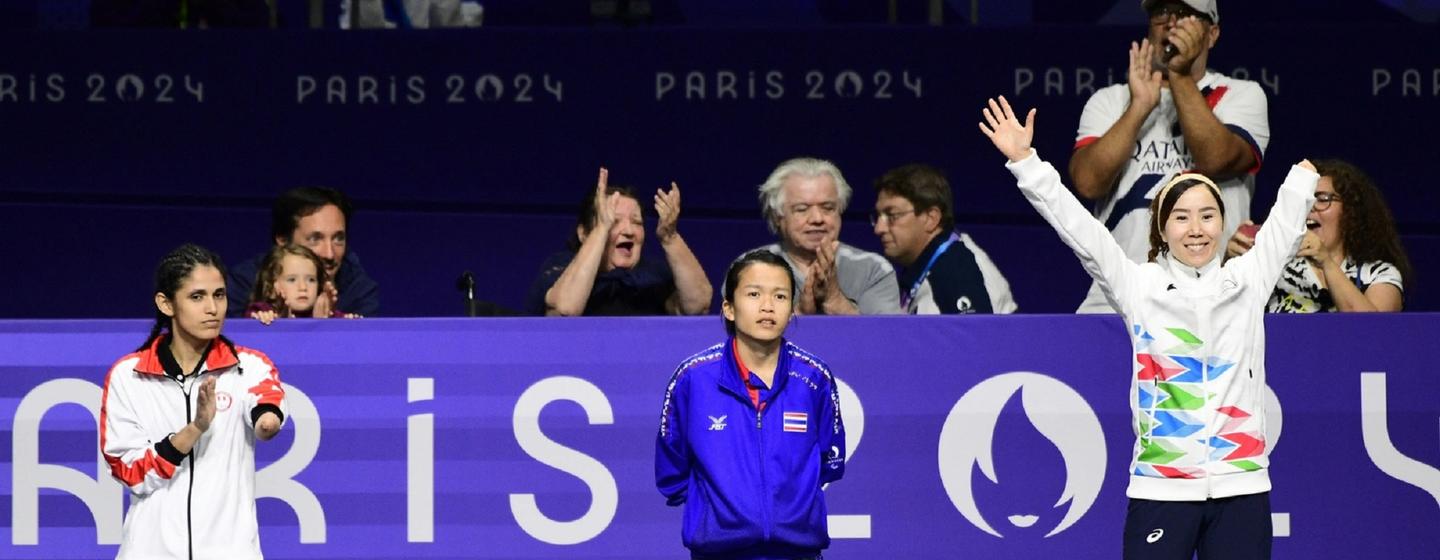 Cérémonie de remise des médailles aux Jeux paralympiques de Paris 2024. Zakia Khudadadi, athlète de l'équipe paralympique des réfugiés, est à gauche sur le podium, entourée du médaillé de bronze au centre et du médaillé d'or à droite. Des spectateurs sont visibles en arrière-plan.