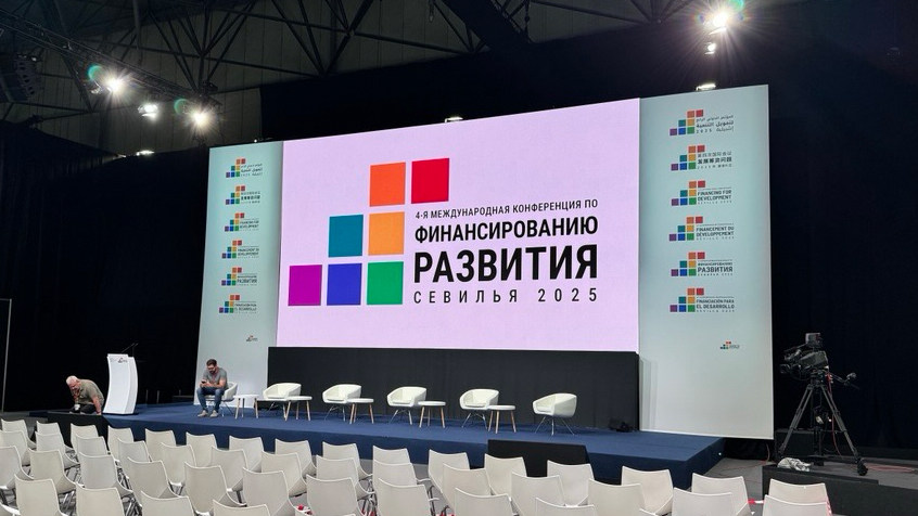 Конференц-зал в Севилье, 2025 год, с большим экраном, на котором на русском языке отображается название мероприятия: «Финансирование развития».