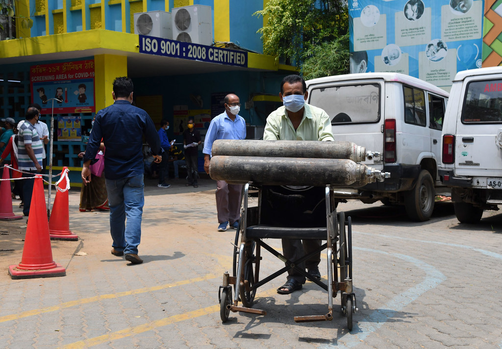 Um homem usando máscara empurra uma cadeira de rodas carregada com dois grandes cilindros de oxigênio em um hospital em Guwahati, na Índia, durante a pandemia de COVID-19.