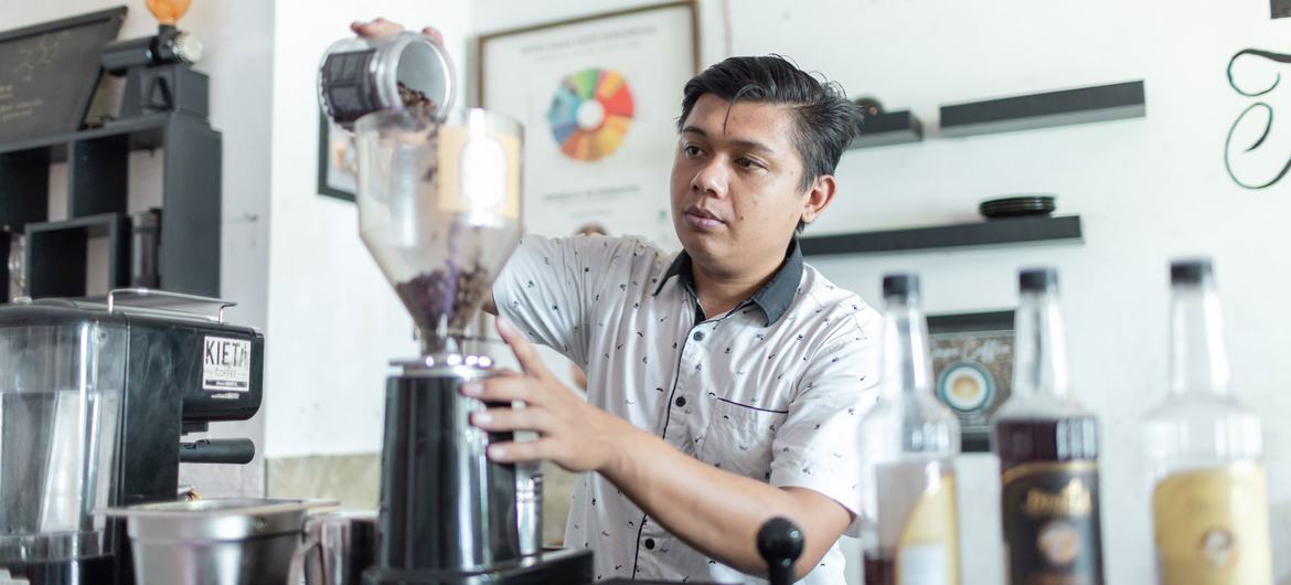 Um detento do sexo masculino em um presídio na Indonésia coloca grãos de café em um moedor como parte de um programa de treinamento profissional.