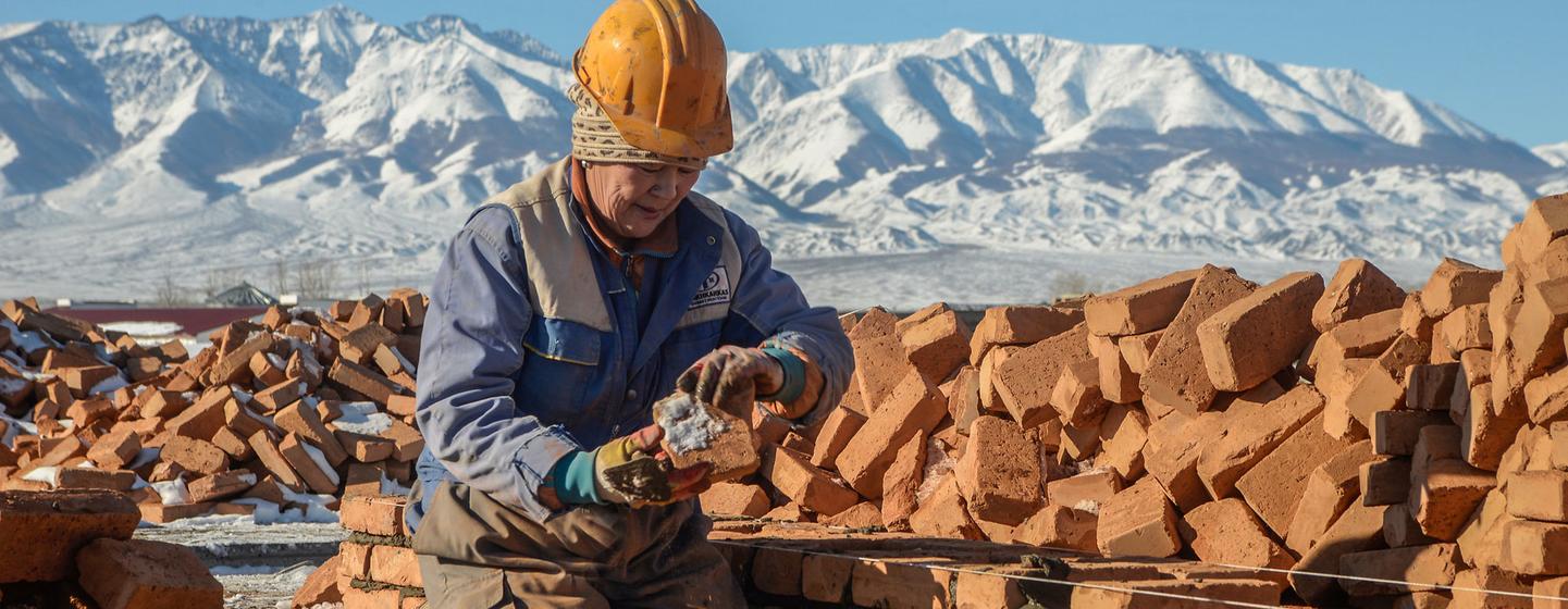 Une ouvrière du bâtiment en Mongolie pose des briques, avec des montagnes enneigées en arrière-plan.