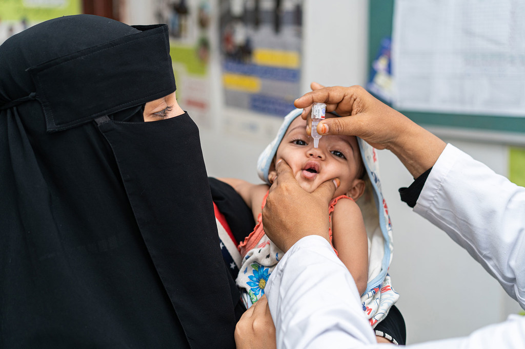 Une mère tient son nourrisson dans ses bras tandis qu'un agent de santé lui administre un vaccin oral dans un établissement médical au Yémen.