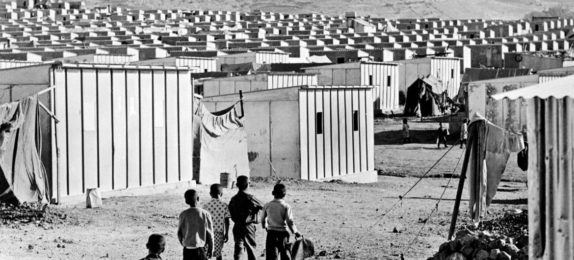 Watoto hutembea katika kambi ya wakimbizi huko Jordan, 1972, ambapo vibanda vilivyotengenezwa tayari vimebadilisha mahema ya turubai.